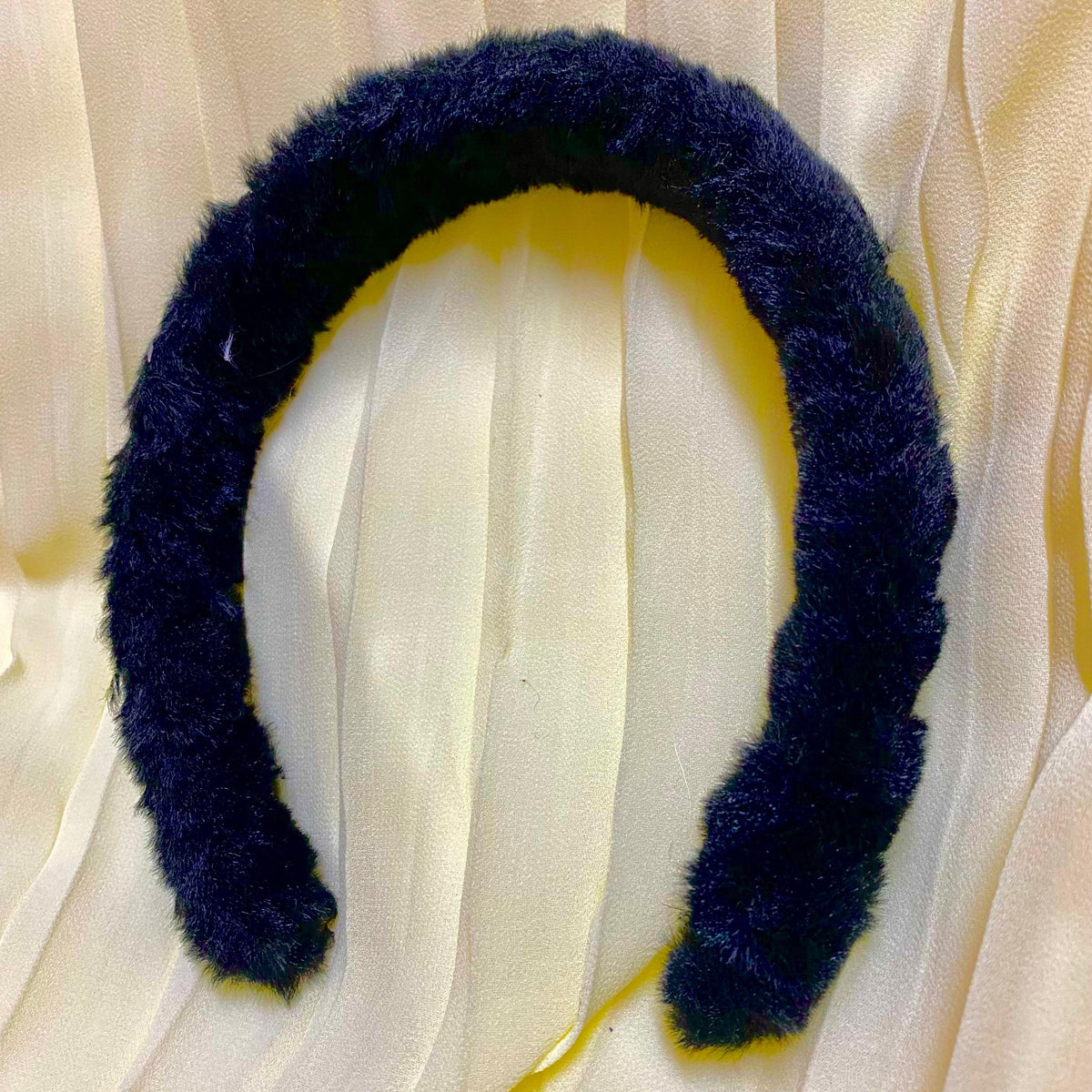 Navy blue fuzzy headband on a beige fabric background