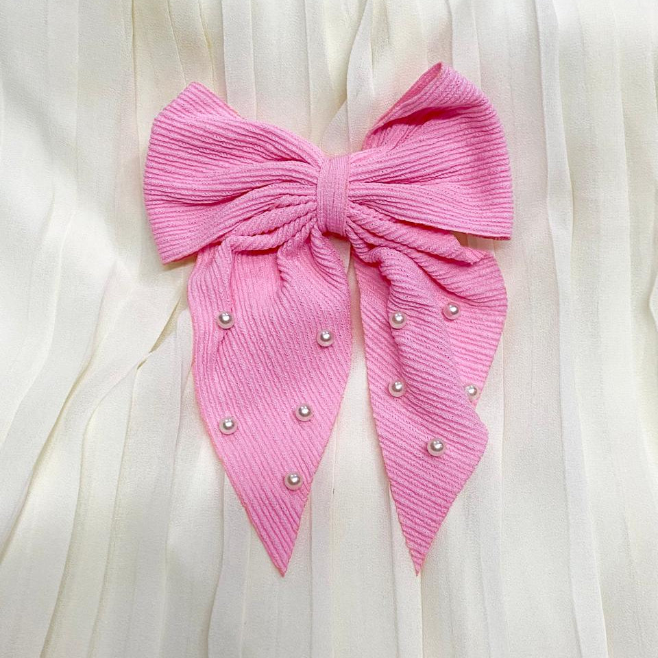 Pink bow with pearl embellishments on a white fabric background