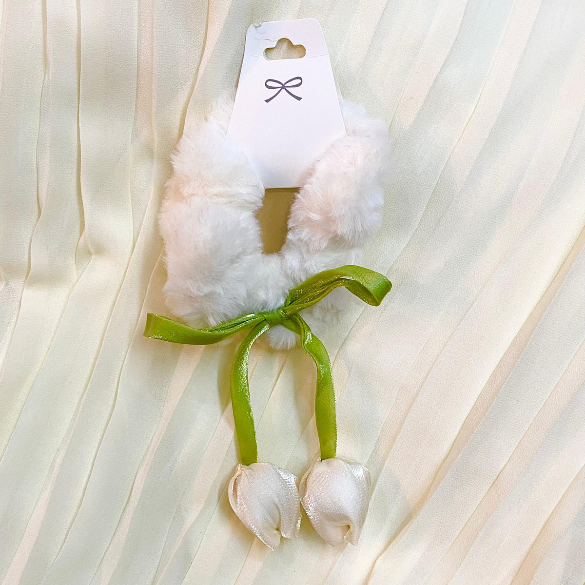 White fluffy toy with a green ribbon on a white fabric background