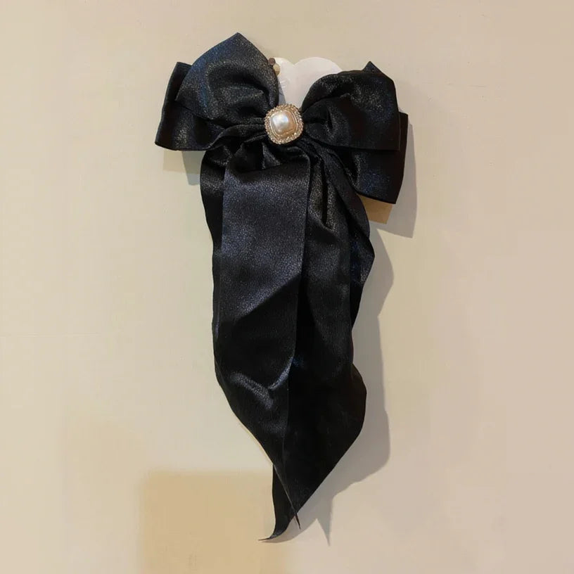 Black satin bow with a pearl center on a beige background